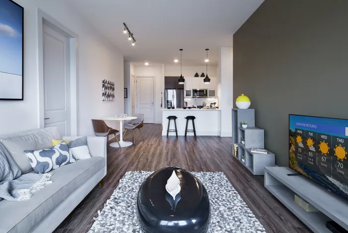 Modern open-concept living room with elegant seating, stylish decor, and a sleek kitchen featuring contemporary lighting.