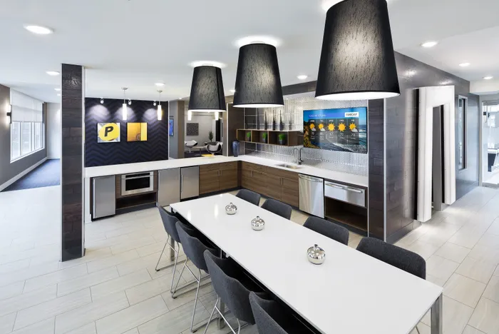 Modern communal kitchen with sleek wooden cabinetry, stylish pendant lighting, and a long dining table, perfect for gatherings.