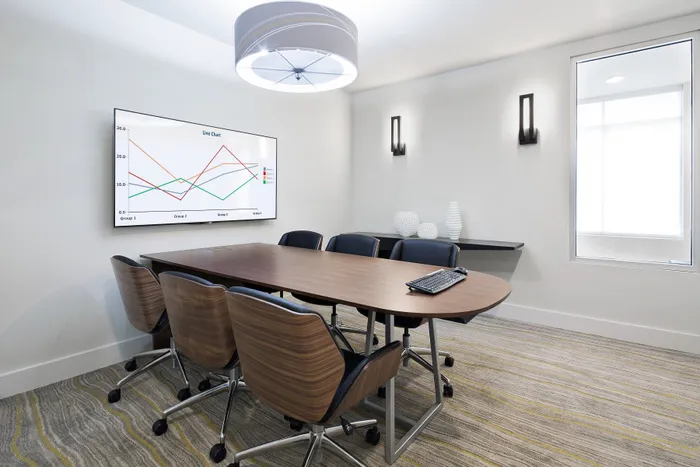 Modern conference room with sleek wooden table, ergonomic chairs, and a large window offering natural light, featuring a wall-mounted screen displaying a line chart for dynamic presentations.