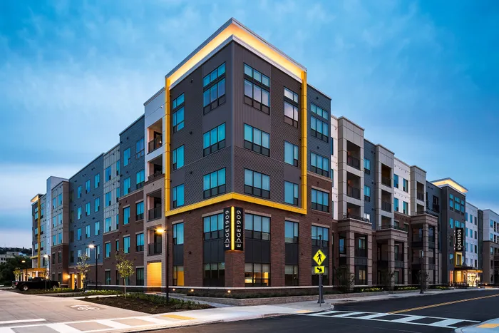 Modern apartment complex with vibrant lighting and contemporary design at dusk, featuring spacious windows and inviting entryways.