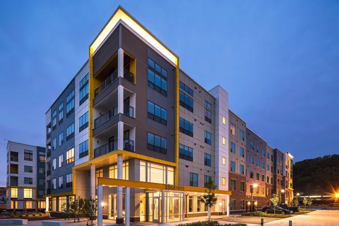 Modern apartment building illuminated at twilight, showcasing sleek architecture with large windows and balconies.