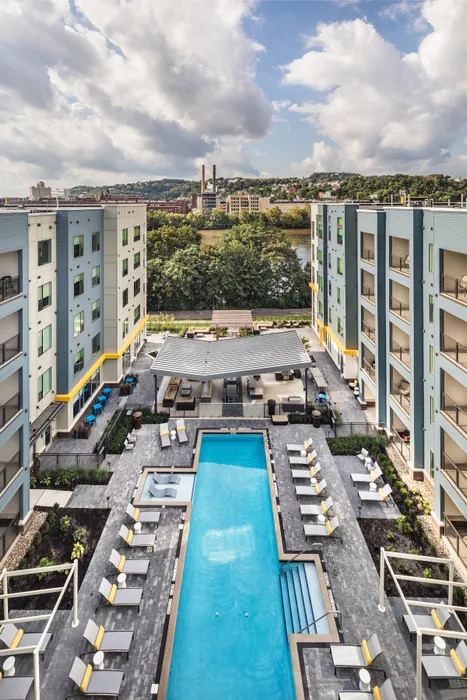 Modern apartment complex with a luxurious pool, inviting lounge chairs, and stunning river views.
