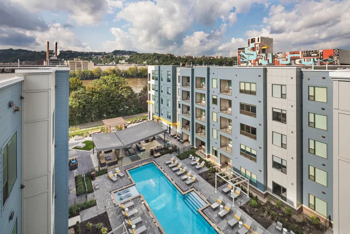 Modern apartment complex with a stunning pool, surrounded by lush greenery and a scenic river view.
