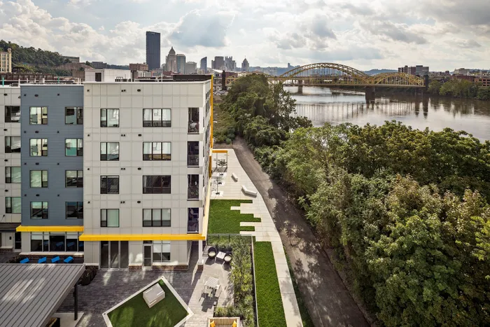 Modern riverside apartment complex with panoramic city and bridge views, featuring beautifully landscaped outdoor spaces.