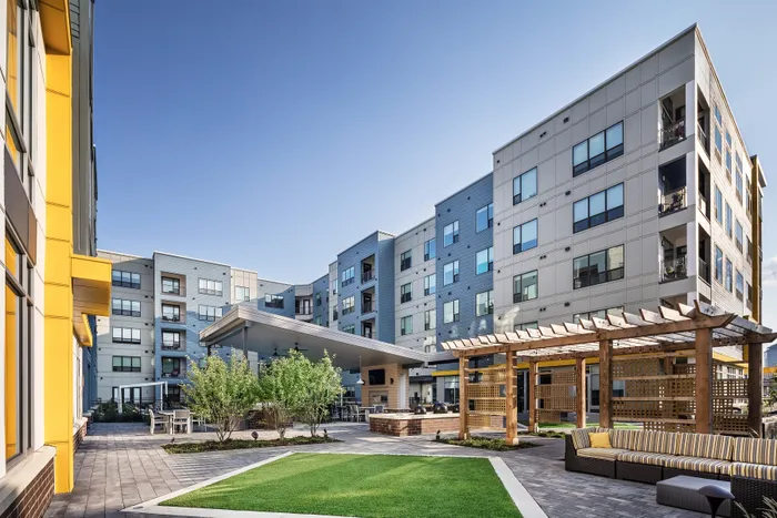 Modern apartment complex with stylish architecture featuring a spacious courtyard, cozy seating area, and vibrant greenery.