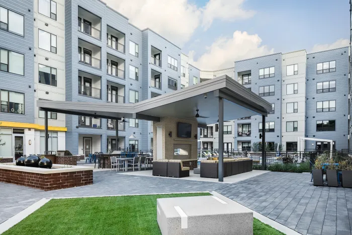 Modern apartment complex with stylish outdoor seating area, dining spaces, and lush green courtyard, perfect for relaxation and entertainment.