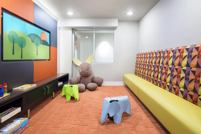 Vibrant children's playroom with a colorful geometric bench, plush bunny, and playful elephant chairs on a cozy brick-patterned carpet.