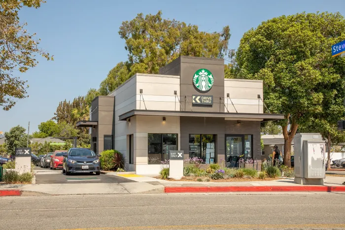 Modern drive-thru coffee shop with sleek exterior design, surrounded by lush greenery and sunny skies.