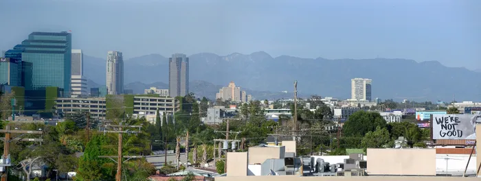 Breathtaking cityscape view featuring modern skyscrapers and lush greenery against a backdrop of majestic mountains.