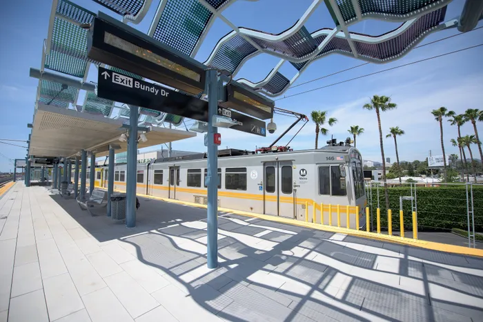 Modern transit station with sleek train under stylish canopy, bathed in bright sunlight with palm trees in the background.