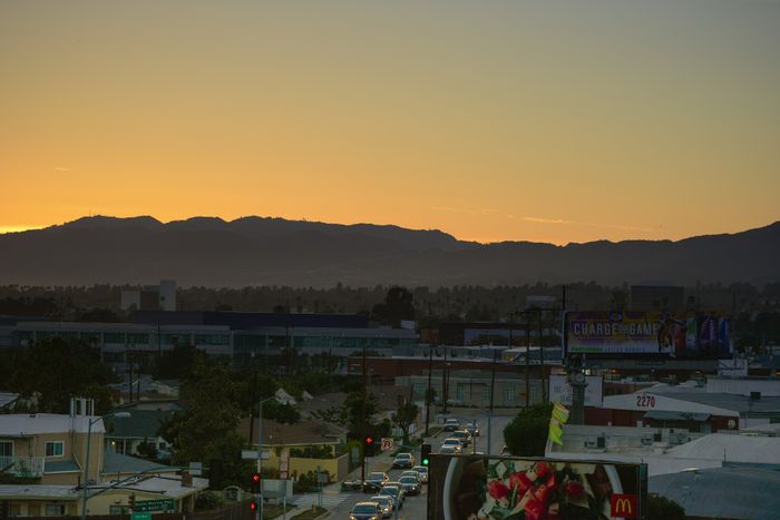Breathtaking sunset view over a bustling urban landscape, with mountains silhouetted against a vibrant orange sky.