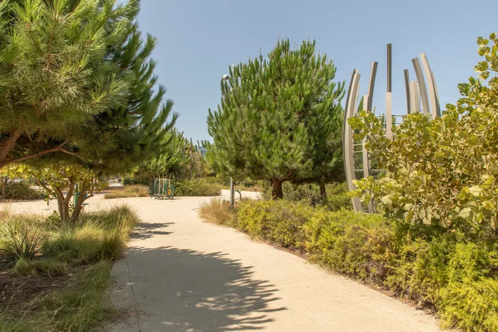 Serene garden walkway featuring lush trees and modern architectural sculptures under a clear blue sky.