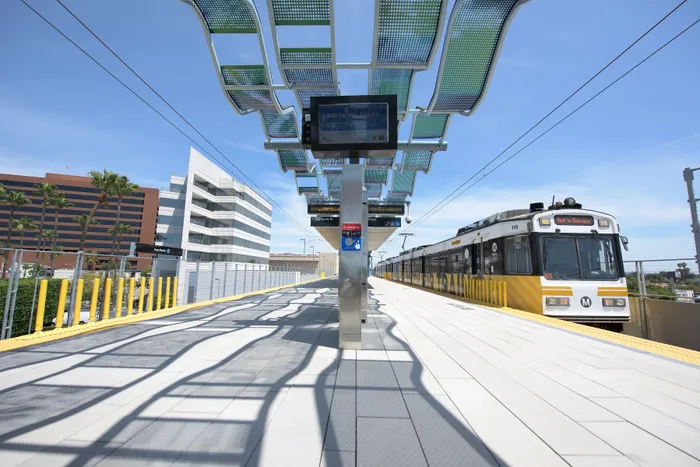 Modern train station with sleek architectural design, featuring a sunlit platform and high-tech transit train under a clear blue sky.