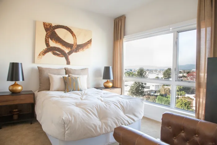 Bright and inviting bedroom with a large window offering scenic views, tasteful artwork, and elegant modern furnishings.