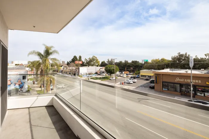 Chic apartment balcony offering a vibrant city view with palm trees and a bustling street, perfect for urban living enthusiasts.