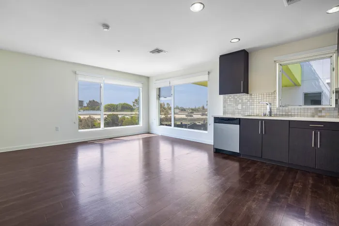 Bright and modern open-concept kitchen and living area with large windows, dark wood floors, and sleek cabinetry offering a stunning view.
