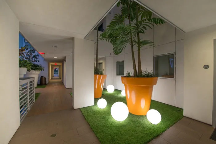 Chic apartment hallway with vibrant orange planters, lush greenery, and modern illuminated spheres creating a welcoming and stylish atmosphere.
