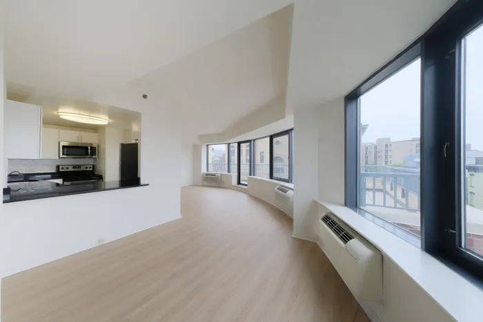Bright, modern open-plan living area with large windows, sleek kitchen, and light wood flooring, offering city views and abundant natural light.