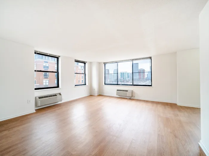 Sunlit spacious living room with large windows offering a stunning cityscape view, featuring elegant hardwood floors and modern design.