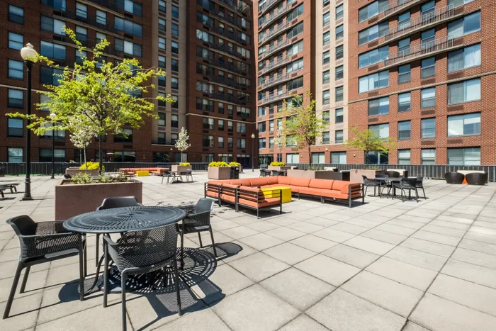 Vibrant urban courtyard with modern seating and lush trees, set against a backdrop of stylish apartment buildings.