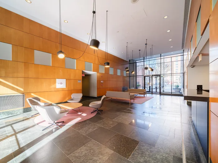 Modern and inviting apartment lobby with sleek design, natural lighting, and stylish furniture, featuring large windows and contemporary light fixtures.