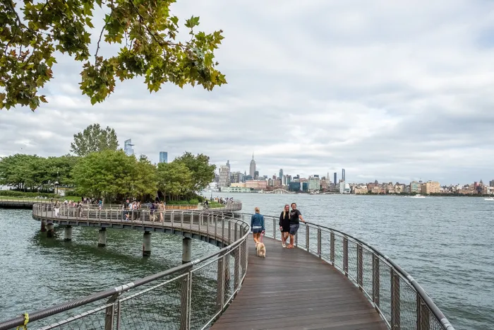 Scenic riverside walkway with lush greenery, stunning city skyline, and people enjoying a leisurely stroll.