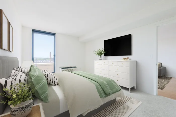Elegant bedroom with modern decor, featuring a plush bed adorned with green and striped pillows, a sleek white dresser topped with greenery, and a wide window offering city views.