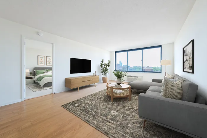 Three-Bedroom Luxury Apartments In Hoboken, NJ - 77 Park Avenue - A Bright, Modern Living Room With A Grey Sectional Sofa, Light Wood Floors, And A Large Window Showcasing A City Skyline.