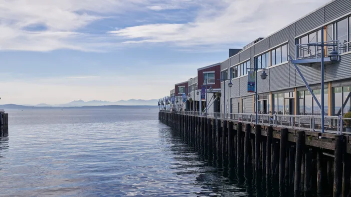 Modern waterfront buildings with expansive windows overlooking serene ocean and distant mountains, offering stunning views and a tranquil atmosphere.