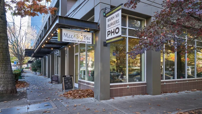 Charming street view of Mee King Bar, an inviting Asian fusion restaurant with modern glass windows, nestled amidst colorful autumn foliage.