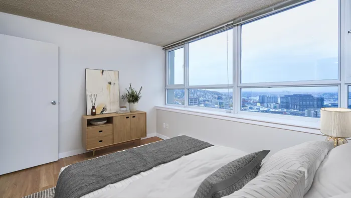 Bright bedroom with modern decor and expansive city view from large windows.