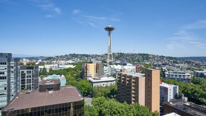 Vibrant cityscape view with iconic tower and modern buildings surrounded by lush greenery under a clear blue sky.