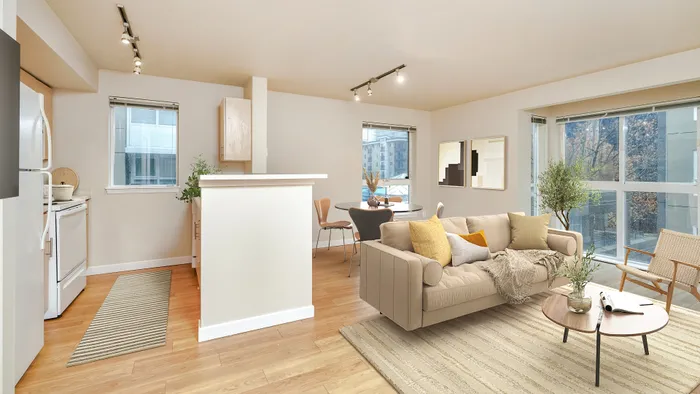 Bright and modern open-concept apartment living room with a cozy sofa, accent chairs, stylish dining area, and a sleek kitchen. Large windows provide abundant natural light and a view of the cityscape.