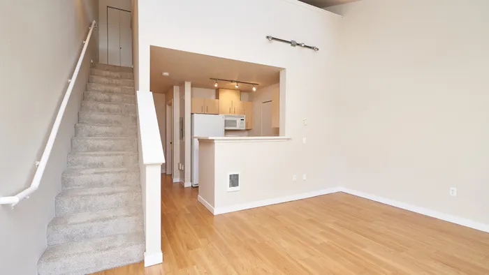 Inviting open-plan living area featuring hardwood floors, modern kitchen, and elegant staircase leading to upper level.