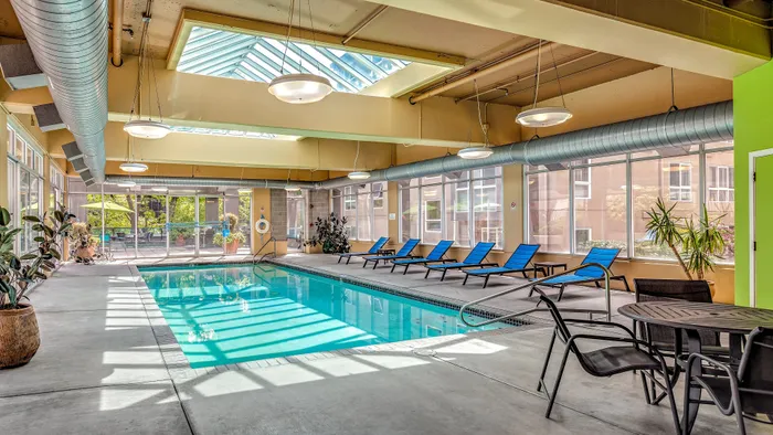 Belltown, WA, Pet-Friendly Luxury Apartments - Centennial Tower and Court - Indoor Swimming Pool with Blue Loungers, Table, Chairs, Large Windows, and Skylight Ceiling.