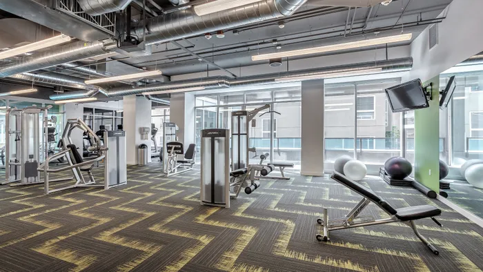 Pet-Friendly Luxury Apartments in Belltown, WA - Centennial Tower and Court - Fitness Center with Strength Training Equipment, Weight Benches, Exercise Balls, Mirrors, Mounted TV, and Large Windows.