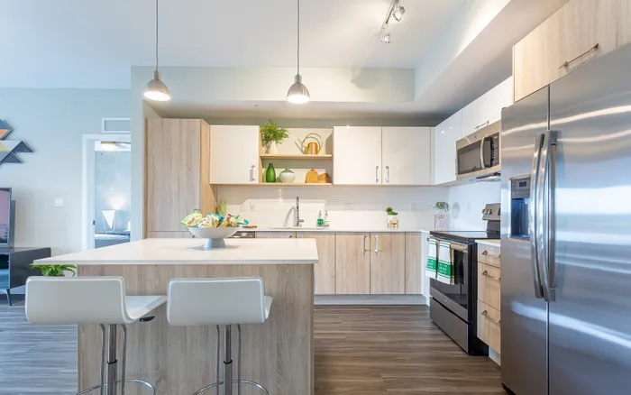 Modern kitchen with sleek appliances, stylish wooden cabinetry, bright lighting, and inviting bar seating. Ideal for contemporary living.