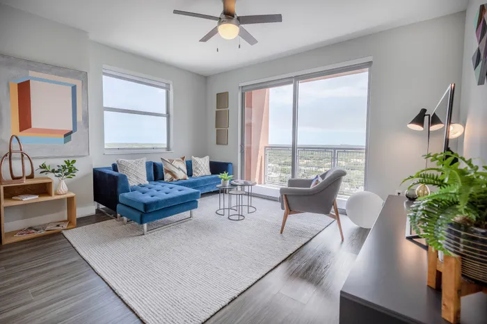 Bright and modern living room with a plush blue sofa, elegant decor, and large windows showcasing stunning city views.