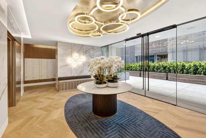 Luxurious apartment lobby featuring elegant marble walls, modern light fixtures, and a chic circular table with vibrant orchids, overlooking a lush green terrace.