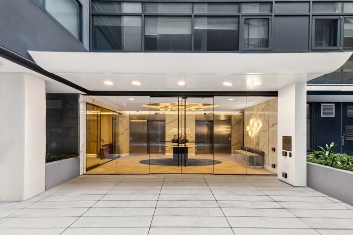Elegant building entrance featuring glass doors, modern lighting, and luxurious stone accents.