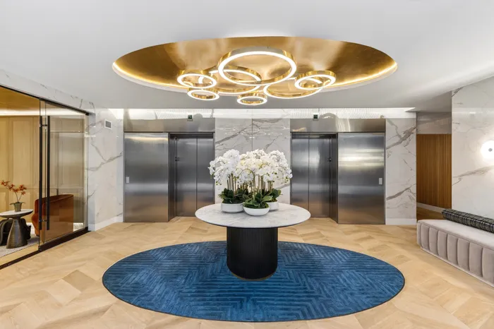 Luxurious lobby with contemporary design featuring a round marble table, elegant orchids, modern lighting, and polished elevators on marble walls.