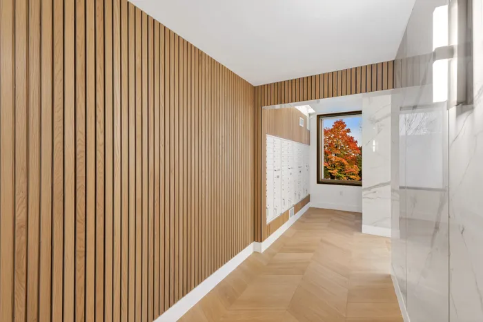Modern entryway featuring stylish wooden paneling, secure mailboxes, and a vibrant tree view through a large window.
