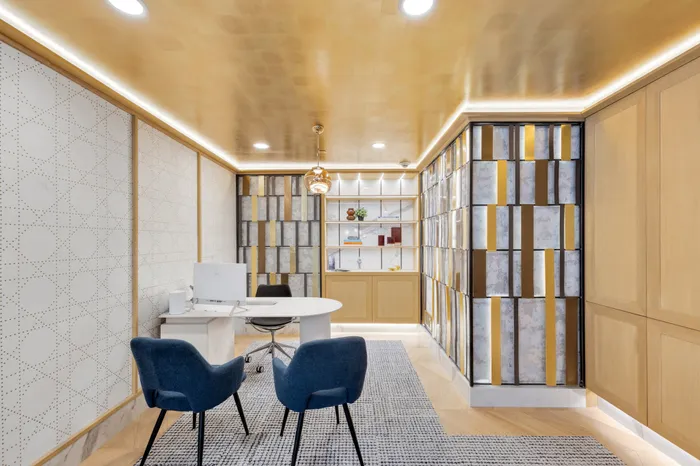 Elegant office space with modern design featuring blue chairs, a sleek white desk, and artistic wall decor under warm lighting.