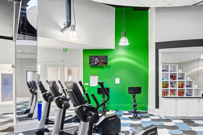 Bright and modern fitness center featuring cardio equipment, vibrant green accent wall, and wall-mounted TV for entertainment.