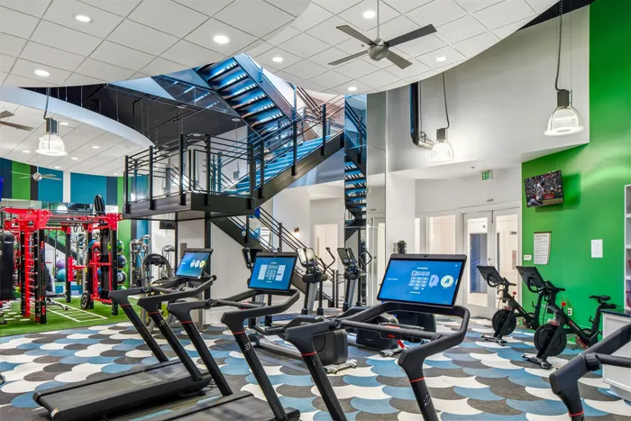 Modern fitness center with state-of-the-art treadmills, vibrant green accent walls, and sleek mezzanine stairway, designed for ultimate workout experience.