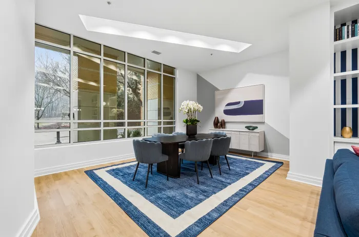 Bright and elegant dining area with large windows, modern furnishings, and stylish decor on a chic blue rug.