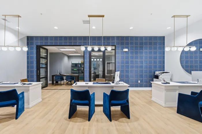 Sophisticated office space featuring modern white desks, plush blue chairs, and stylish lighting fixtures against a chic blue patterned wall.