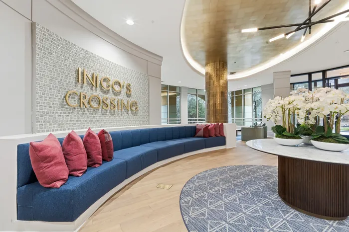 Luxurious lobby of Ingo's Crossing featuring a stylish curved blue sofa with elegant red pillows, a chic gold column, and a modern chandelier, creating a warm and inviting atmosphere.