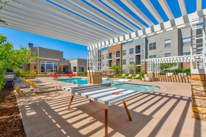 Modern outdoor area with a refreshing pool, stylish lounge chairs, vibrant seating, and shaded pergolas, perfect for relaxation and leisure.