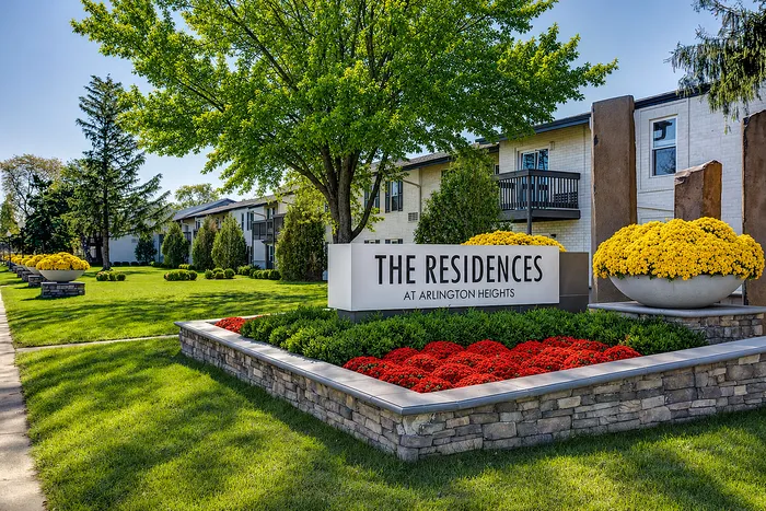 Lush landscaped entrance at The Residences at Arlington Heights featuring vibrant flower beds, mature trees, and modern architecture.